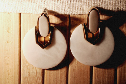 a pair of white and gold earrings hanging on a wall