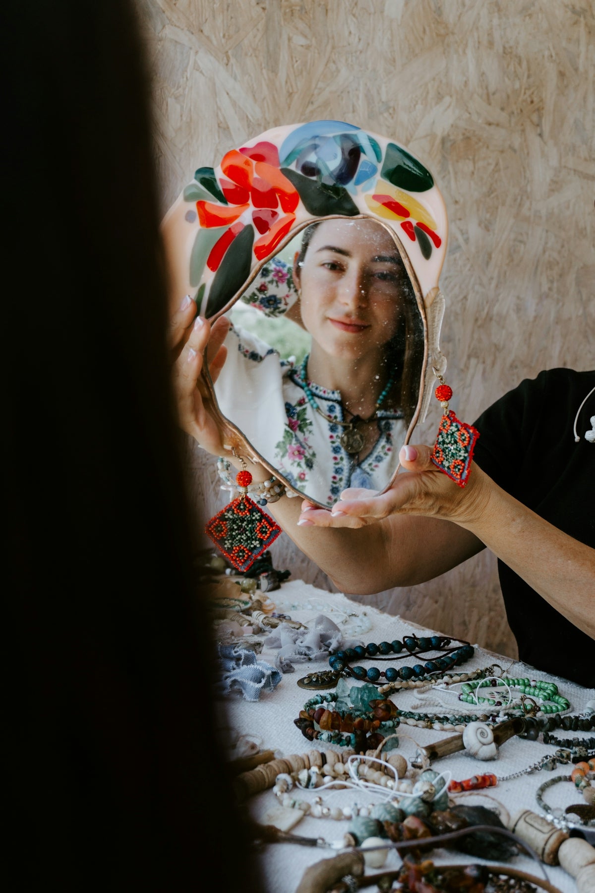 A woman holding a mirror over a table full of jewelry