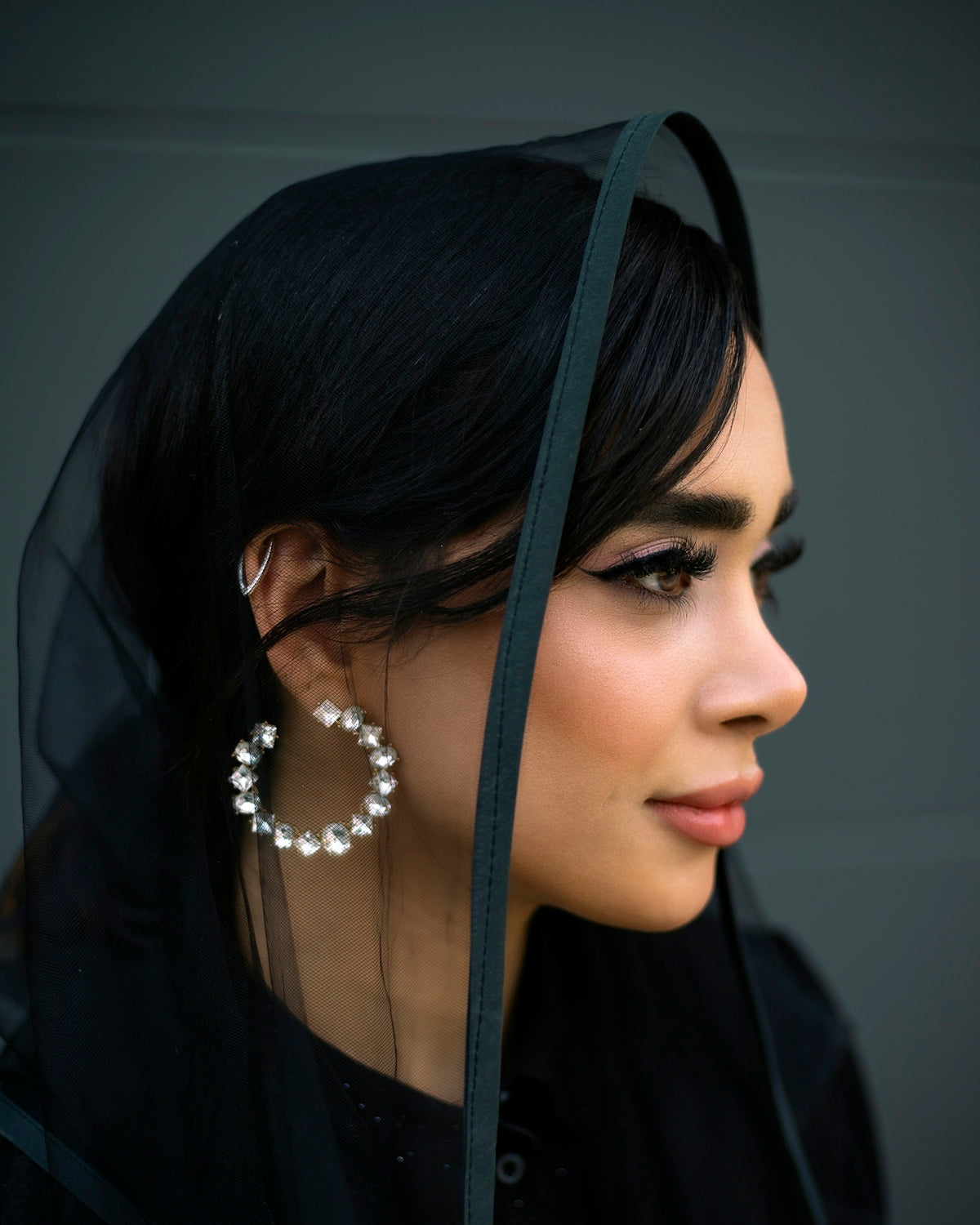 Woman wearing a black hijab and large hoop earrings.