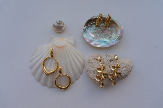 Gold earrings displayed on seashells and coral.